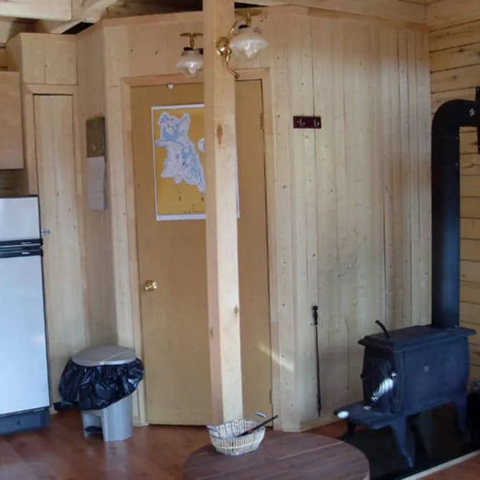 Interior view of the cabin including a wood stove and natural wood paneling walls.