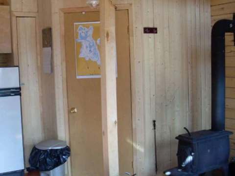 Interior view of the cabin including a wood stove and natural wood paneling walls.