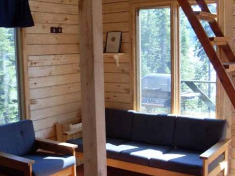The cottage living room features a wooden sofa and armchair near a large window.
