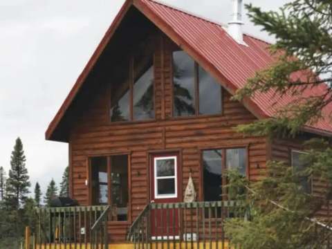 Façade extérieure du chalet en bois avec sa galerie et son toit rouge.