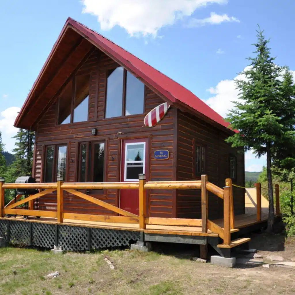 Façade extérieure du chalet en bois avec sa galerie et sa toiture rouge.
