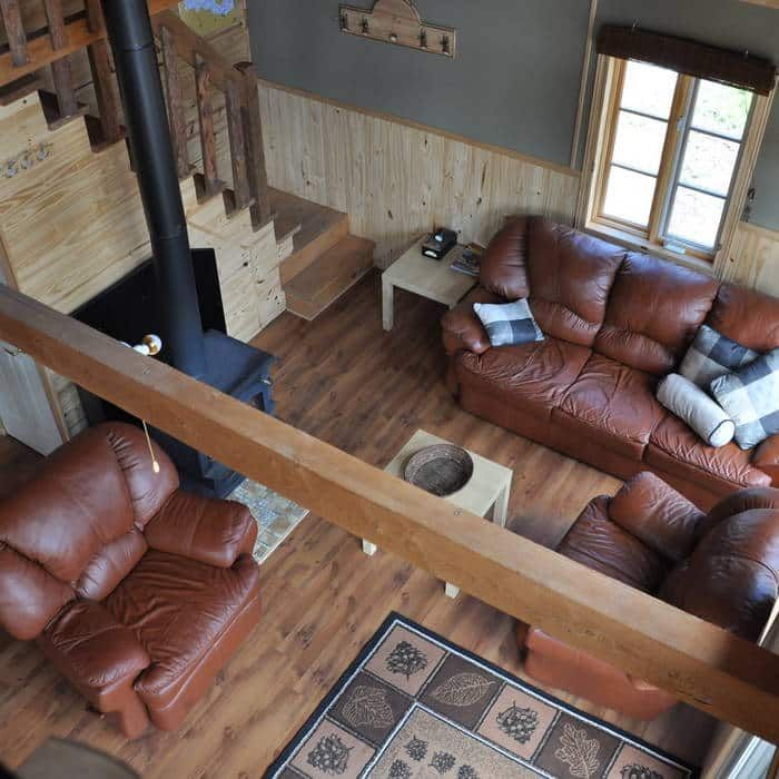 The cottage living room features a fireplace, comfortable leather armchairs, and a wooden staircase.
