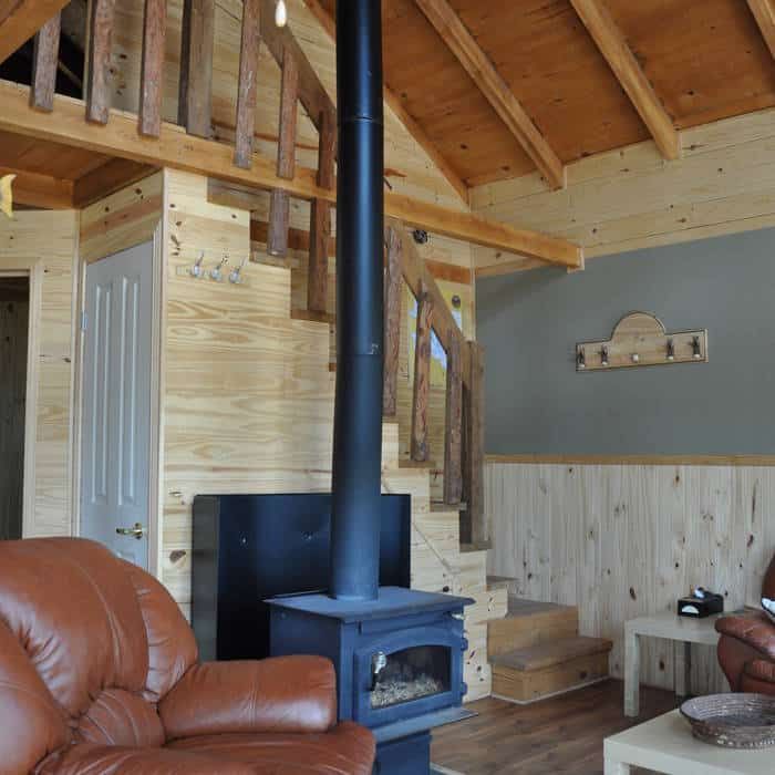 The cottage living room features a central wood stove and a staircase leading to a mezzanine.