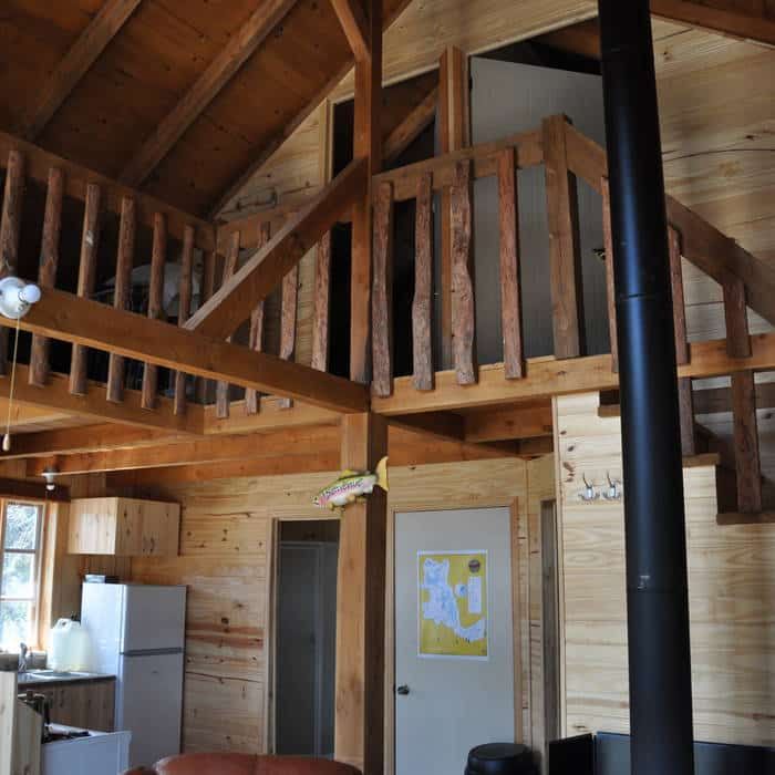 View of the wooden mezzanine and the open-concept kitchen inside the cabin.