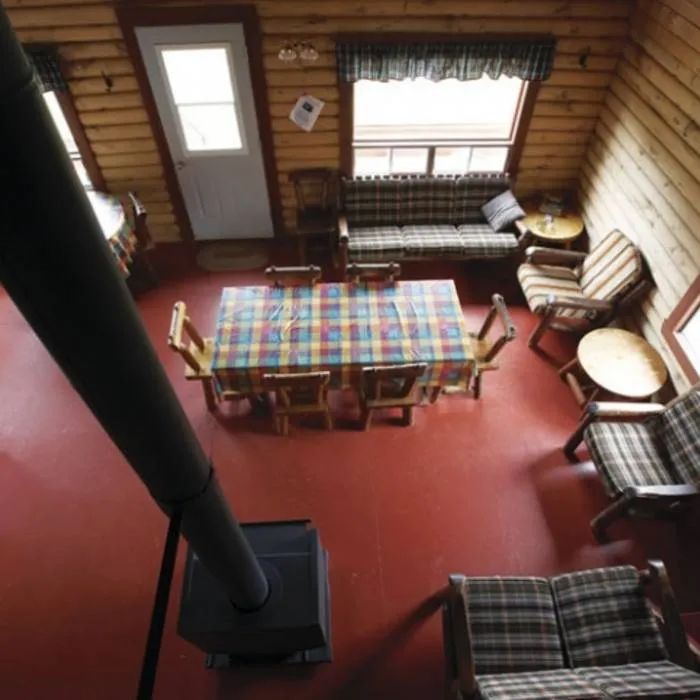 The cottage dining room and living area feature a wood stove and rustic wooden furniture.