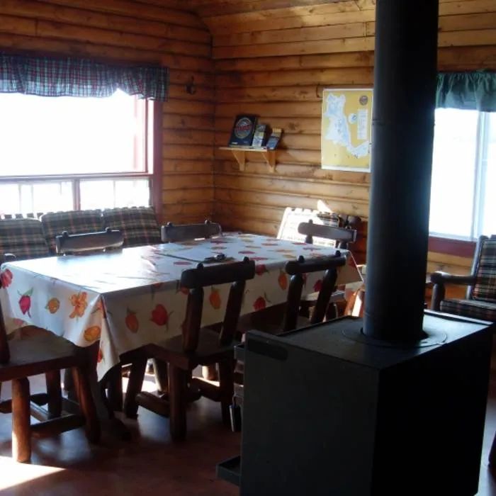 The cottage dining area features a wooden table and a stove to heat the room.