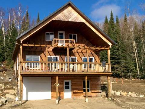 Vue extérieure du chalet Le Panoramique avec son grand balcon et son revêtement en bois.