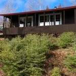 Façade extérieure du chalet Le Canot avec sa véranda entourée de conifères.