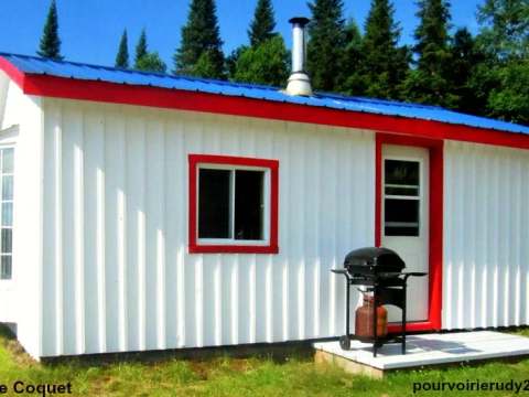 Le chalet Le Coquet est une construction blanche avec un toit bleu située en forêt.