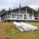 Vue extérieure du chalet Le Familial avec une grande galerie et des embarcations devant.