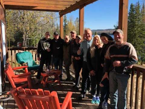 Un groupe profite de la terrasse couverte du chalet avec une vue sur la forêt et le lac.