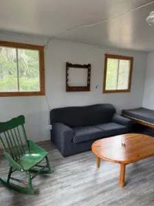 The living area of cabin 12 provides a simple relaxation space with a sofa, rocking chair, and coffee table.