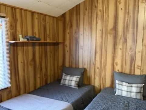This bedroom in chalet 6 is equipped with two single beds featuring gray bedding.