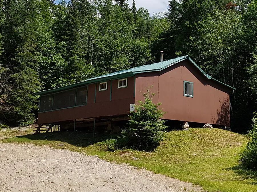 Cabin number 6 is located in the forest and features a screened-in porch.