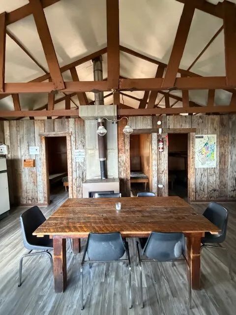 The cottage dining area features a wooden table and a central stove.