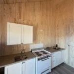 The cottage's equipped kitchen features a stove and white cabinets on wooden walls.