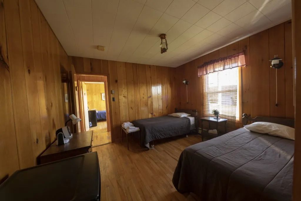 This inn bedroom features two single beds and wood paneled walls.