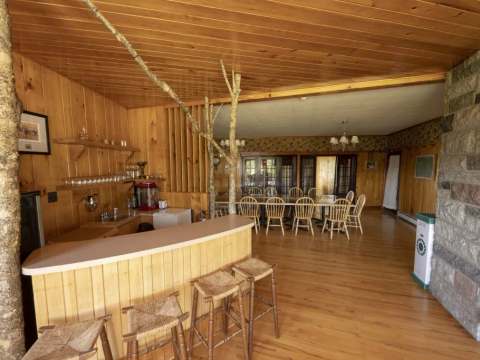 This cozy common room features a bar area, a large dining table, and a stone fireplace.