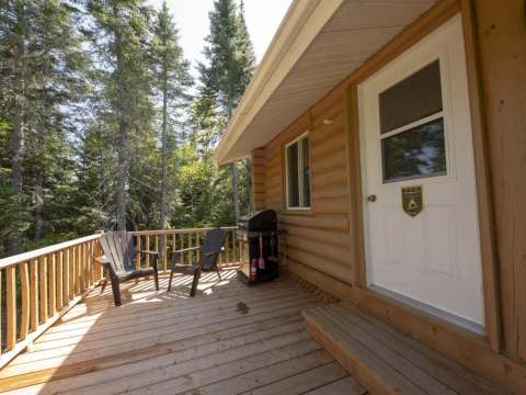 The wooden deck of the cabin is equipped with chairs and a barbecue to enjoy nature.
