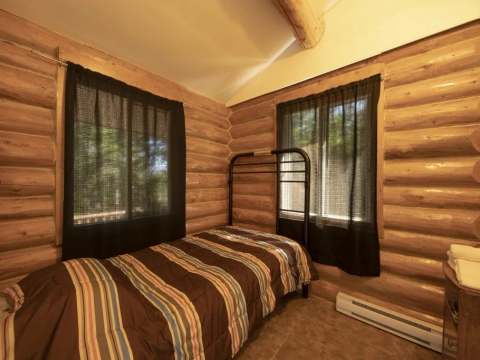 This rustic bedroom with log walls features a comfortable single bed.