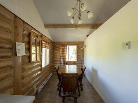 The cottage dining room features a wooden table and log walls.