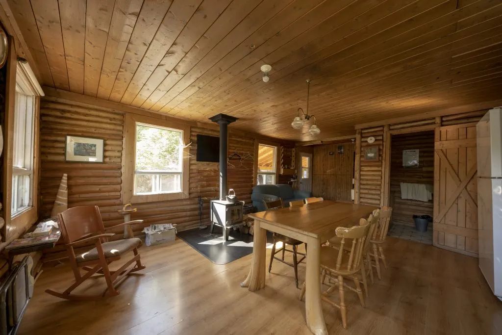 The cottage interior features a dining table, a wood stove, and a cozy sitting area.