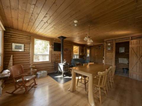 The cottage interior features a dining table, a wood stove, and a cozy sitting area.