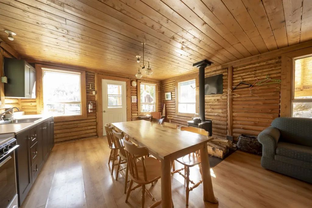 The chalet's open area includes a fully equipped kitchen, a dining table, and a wood stove.