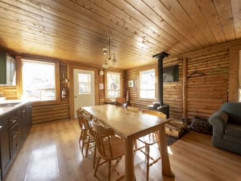 The chalet's open area includes a fully equipped kitchen, a dining table, and a wood stove.