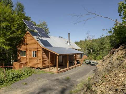 The log cabin is equipped with solar panels and features a covered porch.