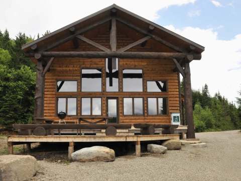 Vue extérieure du Chalet Caché avec sa grande terrasse en bois et ses nombreuses fenêtres.