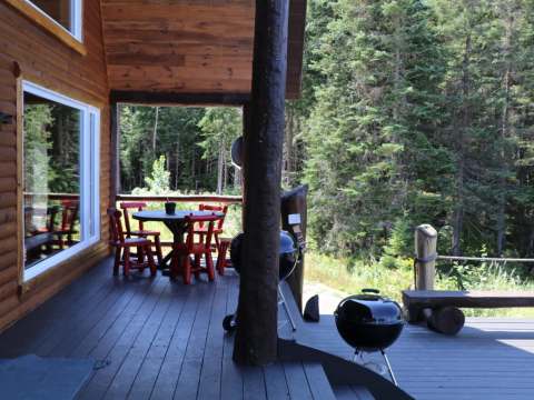 La galerie couverte du chalet dispose d'une table avec des chaises et d'un barbecue pour cuisiner.