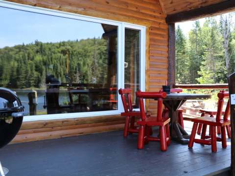 La galerie du chalet offre une vue sur la forêt et un espace avec table et chaises pour manger dehors.