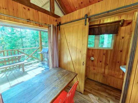 Vue intérieure du mini chalet avec coin repas, porte coulissante et accès à la galerie extérieure.