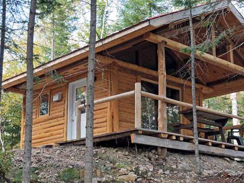 Le mini chalet Le Fisher offre une structure en bois rond avec une terrasse couverte extérieure.