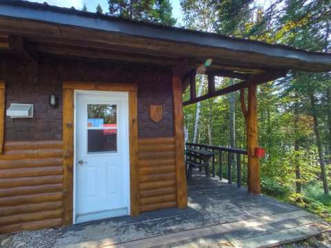 Entrée du mini chalet Oasis avec sa galerie couverte en forêt.
