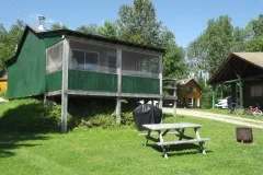 Cabin with screened porch, picnic table, and barbecue on the grounds.