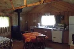 Vue de l'intérieur du chalet avec cuisinette, table à manger et poêle à bois.