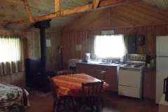 Vue de l'intérieur du chalet avec cuisinette, table à manger et poêle à bois.