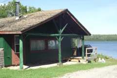 Le chalet 2 de couleur verte est situé sur le bord de l'eau avec une petite galerie extérieure.