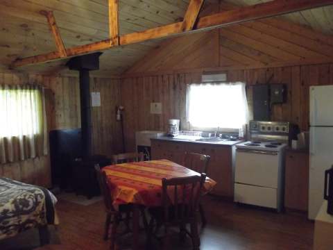 La cuisine et la salle à manger du chalet avec poêle à bois et murs en bois lambrissé.