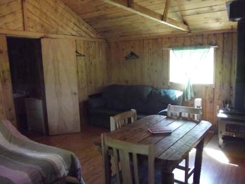 L'aire de vie du chalet comprend une table à manger, un canapé et un poêle à bois.