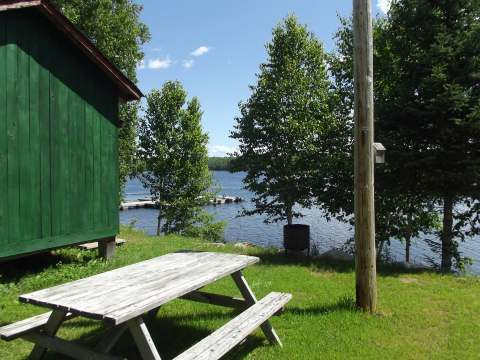 Vue sur le lac et le quai depuis l'extérieur du chalet, avec une table de pique-nique à disposition.