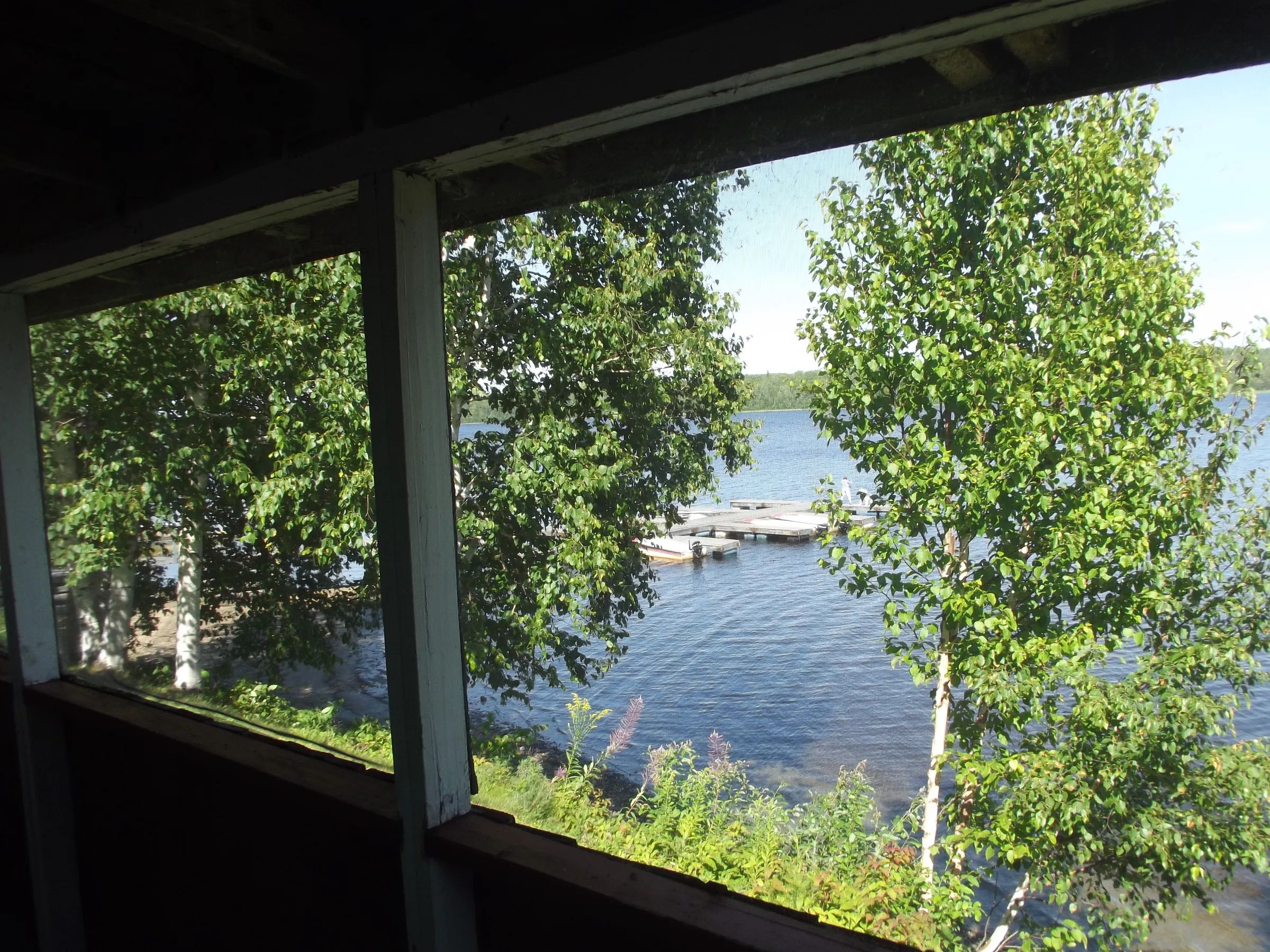 Vue sur le lac et le quai depuis la véranda grillagée du chalet.