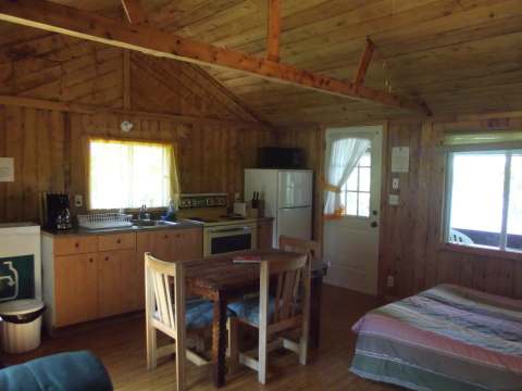 Vue d'ensemble de l'aire ouverte comprenant la cuisine, la salle à manger et le coin lit du chalet.