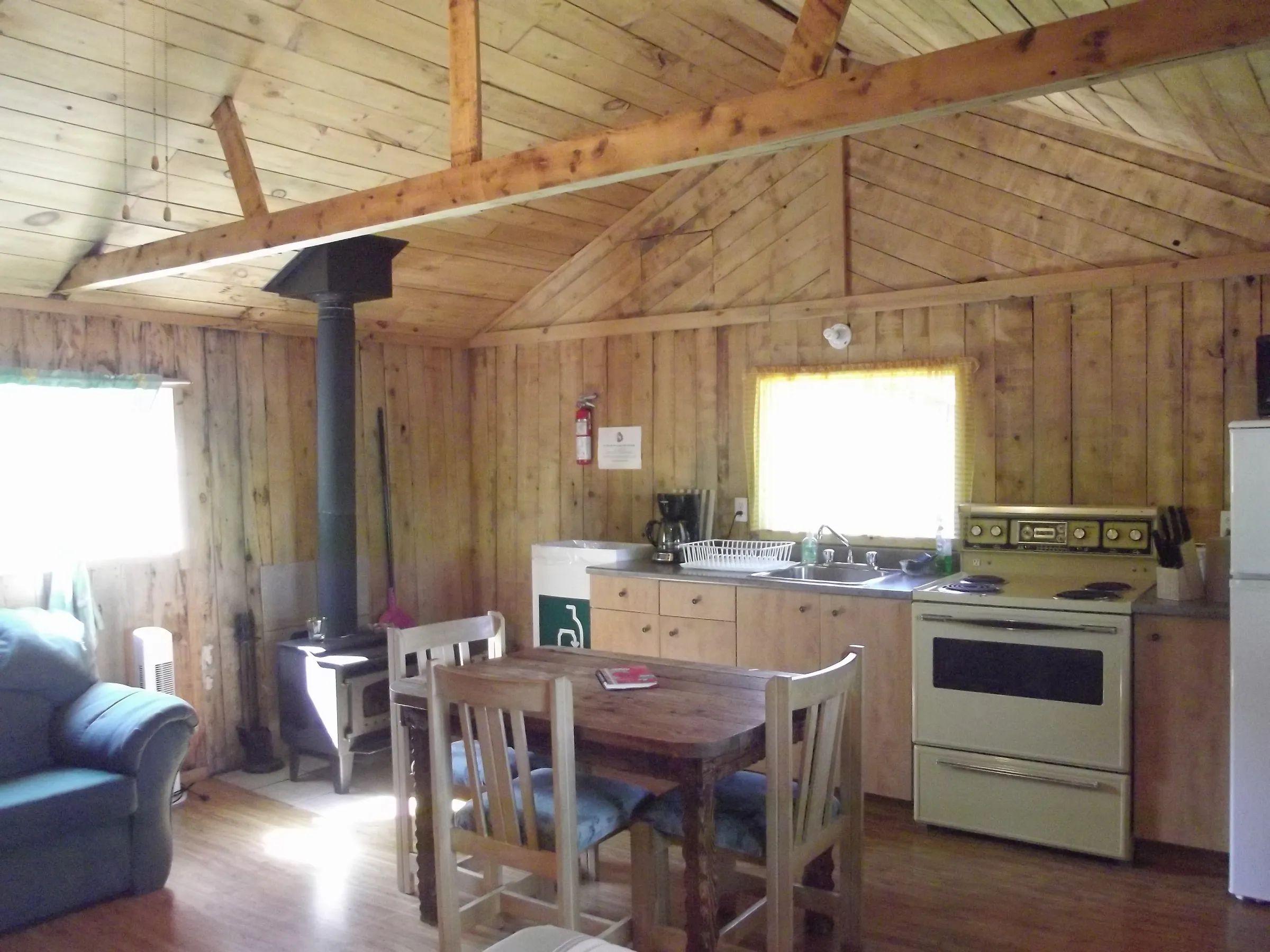 L'aire ouverte du chalet comprend une cuisine équipée, une table à manger et un poêle à bois.