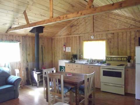 L'aire ouverte du chalet comprend une cuisine équipée, une table à manger et un poêle à bois.