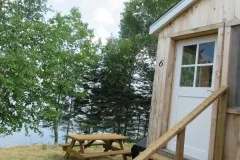 Entrance of cabin 6 with its outdoor picnic table located near the trees and the water.