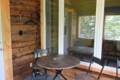 A table and chairs are set up on the small exterior porch of the cabin.