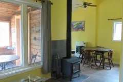 The cabin interior features a wood stove, a dining area, and a view of the covered porch.